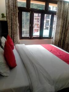 ein Bett mit roten Kissen in einem Schlafzimmer mit Fenster in der Unterkunft Mountain in Dharamshala