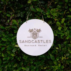 a white sign hanging on a green bush at Sandcastles in Barrack Point