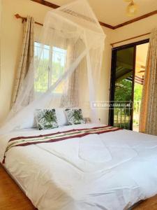 a bedroom with a white bed with curtains and a window at Baan Hug Na in Ban Khao Chakan