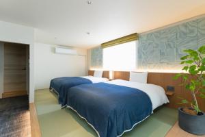 two beds in a room with a potted plant at Nagi Kurashiki Hotel&Lounge in Kurashiki