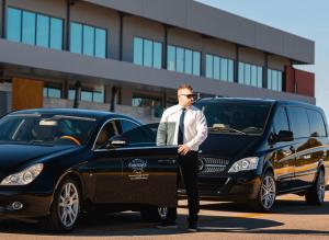 a man in a suit and tie standing next to a car at Emerald Villas & Suites - The Finest Hotels Of The World in Agios Nikolaos