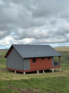 a red barn with a gray roof in a field at Chalet des Gardettes, belle vue 1220m d'altitude in Montgreleix
