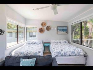 ein Schlafzimmer mit zwei Betten und einer Couch und Fenstern in der Unterkunft SeaRoos by the Seashore Beach Cottage in Durras