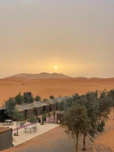 Mustapha Camp Merzouga في مرزوقة: مبنى في الصحراء مع غروب الشمس في الخلفية
