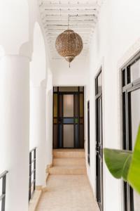 un couloir aux murs blancs et un plafond avec un lustre dans l'établissement Riad La Lumière d'Étoile, à Marrakech