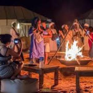 a group of people standing around a fire at desert indigo luxury camp in Merzouga