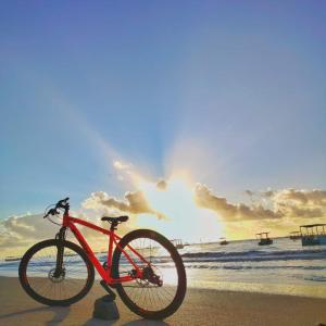 Angá Beach Hotel في ساو ميغيل دوس ميلاجريس: دراجة حمراء متوقفة على الشاطئ مع غروب الشمس