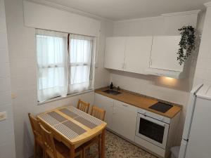 a kitchen with white cabinets and a table with chairs at Piso Frente al Mar, O Barqueiro 2 in O Barqueiro +9 photos