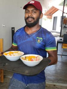 a man holding a tray with two bowls of fruit at Surf And Stay Arugam Bay in Arugam Bay