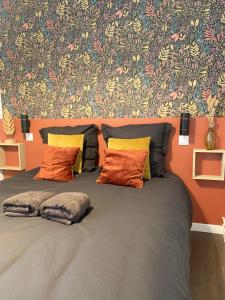 a bed with orange pillows in front of a wall at Le Constantin - Ecrin chaleureux & confortable, centre-ville à 2 pas in Provins