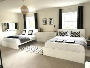 two beds in a white bedroom with a mirror at Stansted Coach House in Elsenham