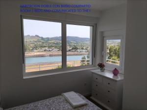 a bedroom with two windows with a view of a river at LA VILLA DE MARIA -CASA MONICA Y GEORGE PLAYA DEL PUNTAL Planta Baja CASA ADOSADA en Villaviciosa ASTURIAS in Villaviciosa