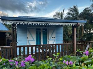 a blue house with a wooden porch with purple flowers at chambres d'hôtes le puits des français in Saint-Philippe