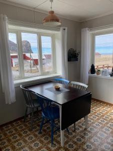 a dining room with a table and chairs and windows at Unstad Surfpacker in Unstad