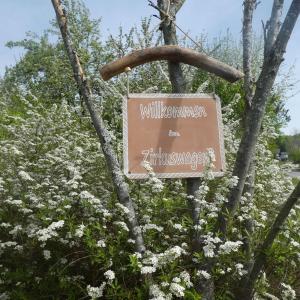 um sinal para a entrada de um parque com flores brancas em Entspannung im Zirkuswagen: außergewöhnliche und liebevoll eingerichtete Glamping-Unterkunft im Grünen em Geigant