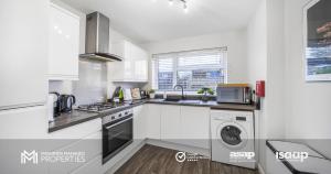 a kitchen with white cabinets and a washer and dryer at Modern 2 Bed Apartment on Edge of City Centre, 2xFREE Private Parking, Ground Floor & Private Entrance in Quiet Neighbourhood in Peterborough