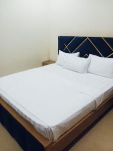 Elle comprend un grand lit avec des draps et des oreillers blancs. dans l'établissement Home Inn Guesthouse, à Islamabad