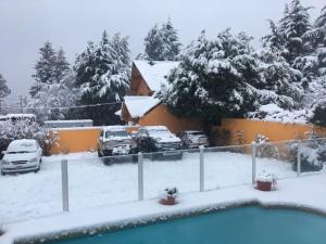 een tuin bedekt met sneeuw met geparkeerde auto's en een huis bij HOTEL LE CHARME con parking in Bariloche