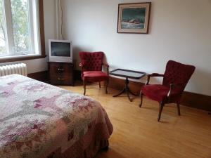 a bedroom with a bed and two chairs and a tv at Le Petit Château Montebello B&B in Montebello