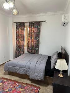 a bed in a bedroom with curtains and a lamp at Quite apartment with positive vibes in New cairo