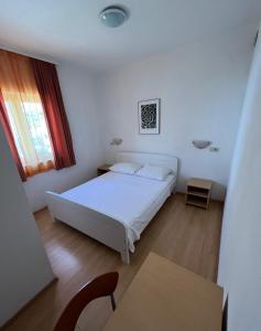a bedroom with a white bed and a table at Apartmani Šaldi in Pakoštane