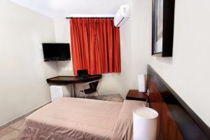 a small room with a bed and a red curtain at Hotel Dom Henrique in Timóteo