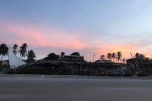 einen Sonnenuntergang über einem Strand mit Häusern und Palmen in der Unterkunft Paraíso do Brutus - casa de temporada in Beberibe