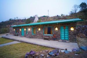 Casa de piedra con ventanas azules y techo verde en Dirghayu Bhava Retreat, en Dehradun