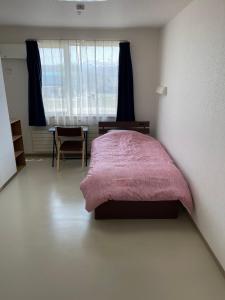 een slaapkamer met een bed met een roze deken en een bureau bij ゲストハウス ikoi in Kyōgoku