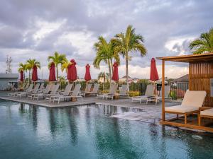 a pool with chairs and red umbrellas and palm trees at Cross Paasha Bali Seminyak in Seminyak