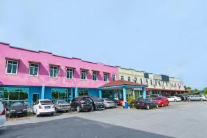 OYO 275 Senyum Inn في بانتايْ سينانج: مبنى وردي مع سيارات متوقفة في موقف للسيارات