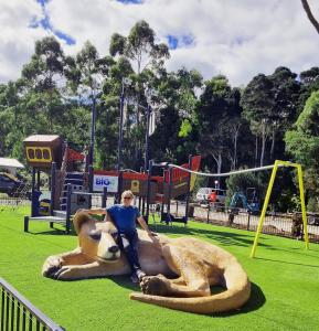 Un homme est assis sur une grande statue de chien dans un parc dans l'établissement BIG4 Strahan Holiday Retreat, à Strahan