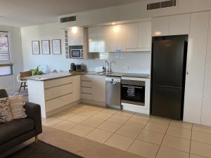 a kitchen with white cabinets and a black refrigerator at Nova Apartment Mooloolaba Beach in Mooloolaba