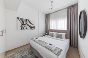 a white bedroom with a large bed and a window at Comfortable 2bd Apartment Next To Metro & Mall in Dubai