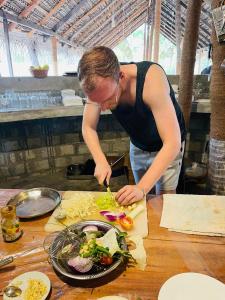 een man die groenten snijdt op een tafel bij Swiss kiss beach resort in Uppuveli