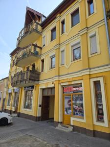 ein gelbes Gebäude auf einer Straße mit einem Auto vor dem Haus in der Unterkunft Júlia Apartman Kaposvár*** in Kaposvár