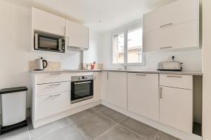 cocina blanca con armarios blancos y microondas en Appartement cosy proche de Paris, en Bagnolet