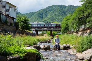 a person sitting on rocks in a river with a train at Kobe Guesthouse MAYA in Kobe