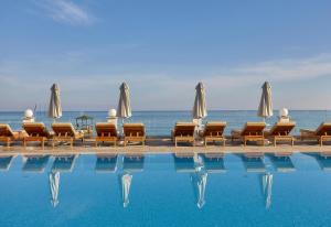 a pool with chairs and umbrellas next to the ocean at Alexander Beach Hotel & Village Resort in Malia