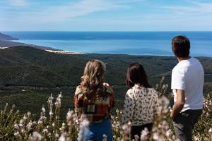 Un gruppo di tre persone in piedi su una collina che guarda l'oceano di L'Aquila ad Arbus