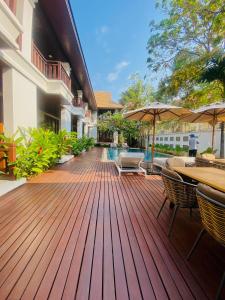 una terraza de madera con sillas, mesas y sombrillas en Athena Hotel en Pakse