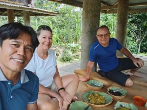 drie mensen zitten rond een tafel met borden eten bij The Twins Homestay in Rantepao