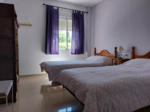 1 dormitorio con 2 camas y una ventana con cortinas moradas en Vivienda Turística Ronda del Carmen, en Bujalance
