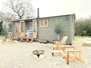 a green tiny house with chairs and a fire pit at Hidden Gem Luxury Shepherd Hut - Pea Pod in Wimbish