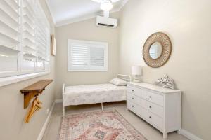 ein weißes Schlafzimmer mit einem Bett und einem Spiegel in der Unterkunft Cathy's Cottage in Cairns