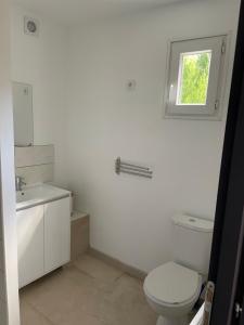 La salle de bains blanche est pourvue de toilettes et d'une fenêtre. dans l'établissement Les Chalets du Mancel : Chalet Lulu - Bouleries Jump - 24h du Mans, à Parence