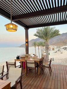 eine Holzterrasse mit einem Tisch und Stühlen am Strand in der Unterkunft Water Front Villa BF108 in Muscat