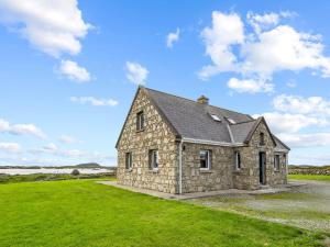 una casa de piedra en un campo de hierba con un cielo azul en Lake House Mannin, Ballyconneely, en Ballyconneely