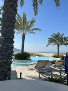 Water Front Villa BF108 في مسقط: مسبح به كراسي و نخيل على شاطئ