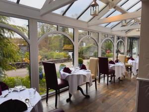 un comedor con mesas y sillas blancas y ventanas en Skelwith Bridge Hotel, en Ambleside